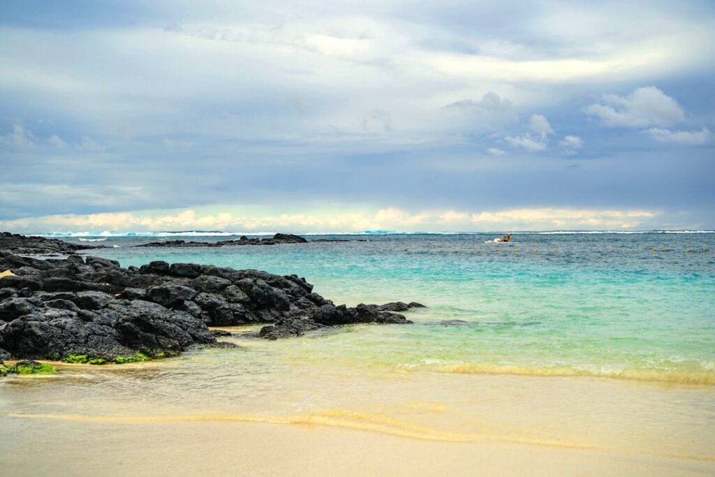 A sandy beach with blue water and rocks