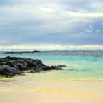 A sandy beach with blue water and rocks