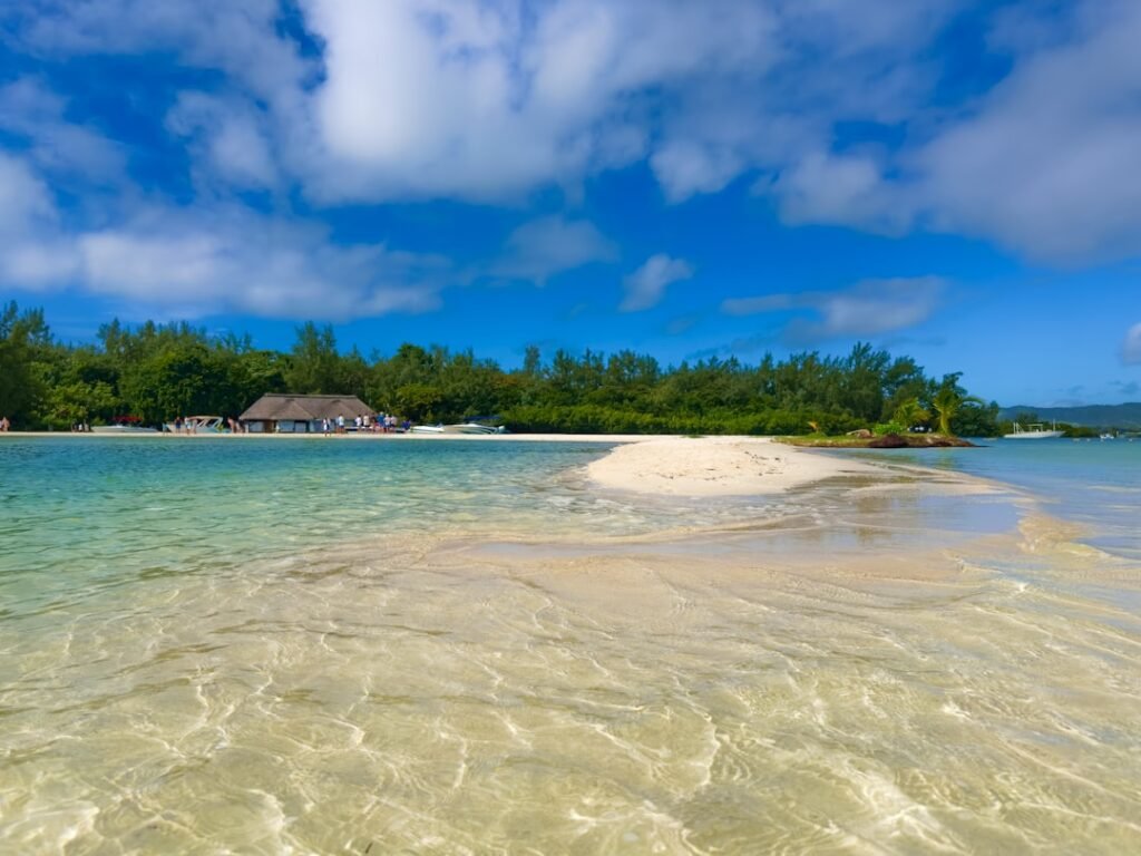 a sandy beach with clear blue water and houses in the background