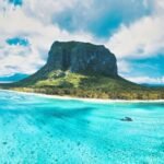 green and black rock formation on blue sea under blue and white cloudy sky during daytime