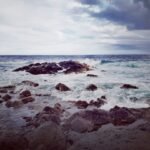 ocean waves crashing on rocky shore under blue and white cloudy sky during daytime