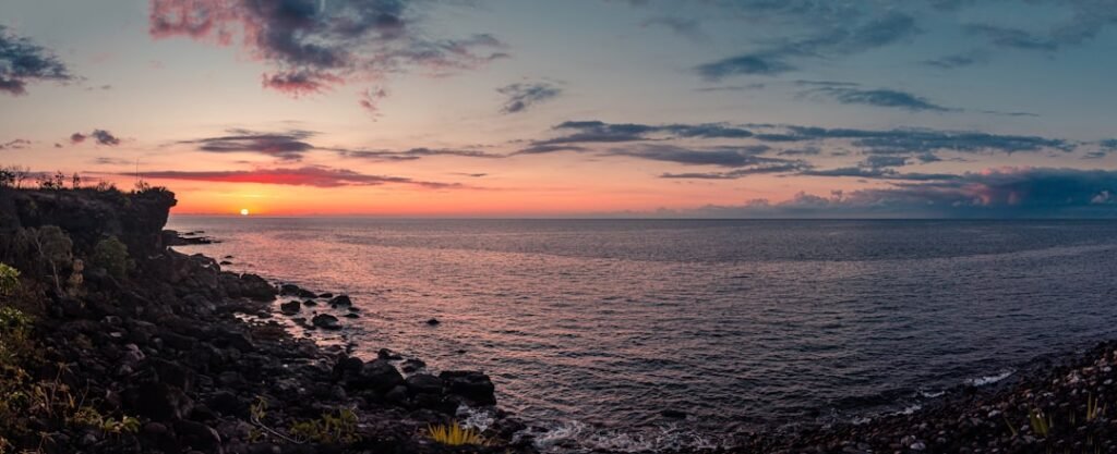 the sun is setting over the ocean on a rocky cliff