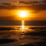 The sun is setting over the water on the beach