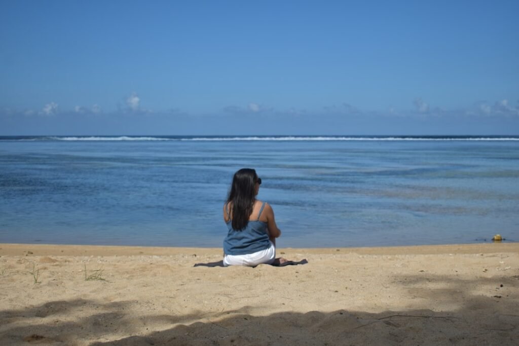 A woman sits on a beach looking at the ocean.