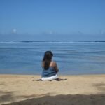 A woman sits on a beach looking at the ocean.