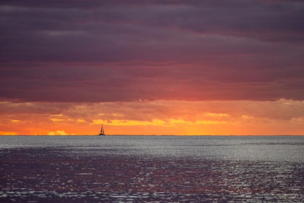 The sun is setting over the ocean with a lighthouse in the distance