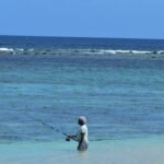 A man standing in the ocean holding a fishing rod