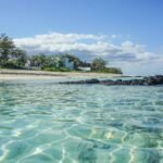 a beach with clear blue water and a white house in the distance